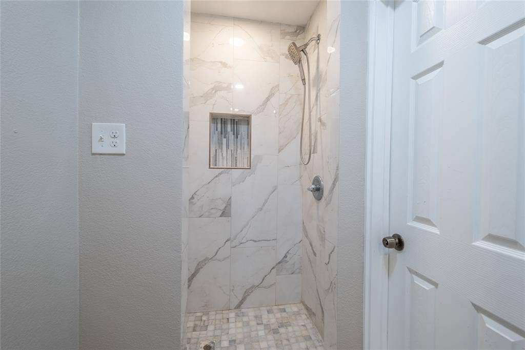 Walk-in shower with large-format tile walls, mosaic tile flooring, a built-in shower niche, and a brushed nickel shower head