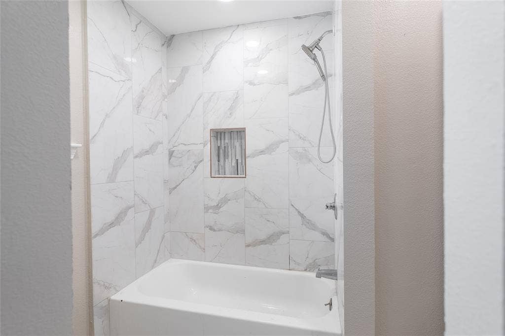 Bathtub with a tiled surround featuring a built-in niche, complete with a showerhead and faucet