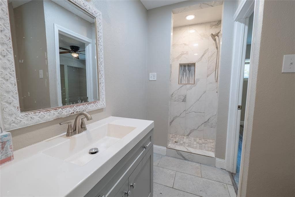 Vanity with integrated sink, brushed nickel faucet, decorative framed mirror, walk-in shower with marble-look tile, and recessed shower niche