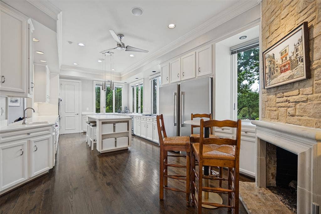 Spacious kitchen featuring extensive white cabinetry, dark wood-finish flooring, a central island with integrated seating, stainless steel appliances, and a stone-clad fireplace