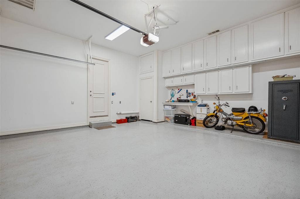 Garage with a light-colored epoxy flooring, extensive built-in white cabinetry, a built-in workbench, and overhead fluorescent lighting