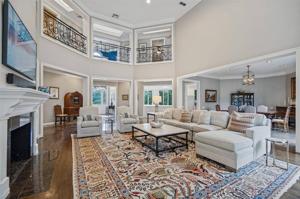 Two-story living area with dark wood-finish flooring, white fireplace, and decorative wrought iron railings