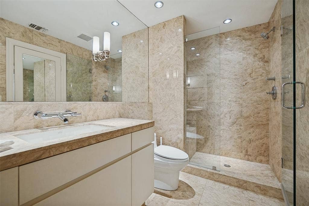 Bathroom featuring extensive stone tile, frameless glass shower enclosure, recessed lighting, and a vanity with an integrated sink