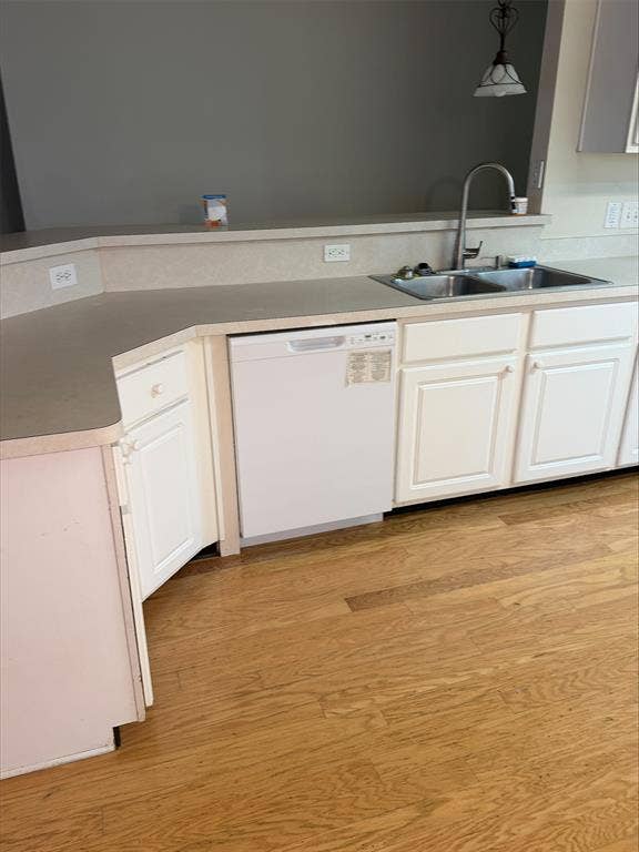 Kitchen featuring white cabinetry, dual basin sink with gooseneck faucet, light-toned countertops, and wood-finish flooring