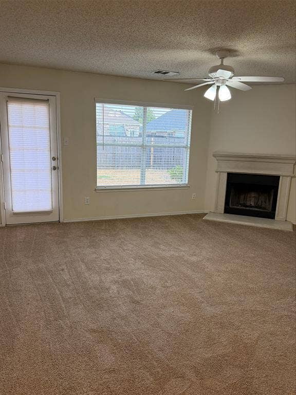 Neutral-toned carpeted flooring, corner-set fireplace with a light-colored mantel, window with horizontal blinds, and a ceiling fan with integrated lighting