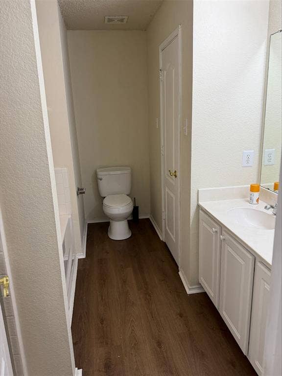 Wood-finish flooring with a white vanity featuring an integrated sink, and a commode