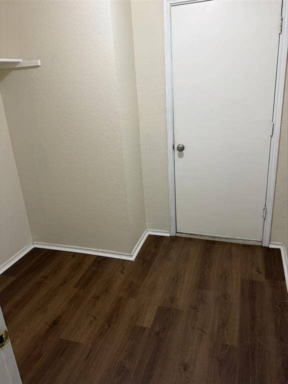 Wood-finish flooring with white trim, a single floating shelf, and a white interior door