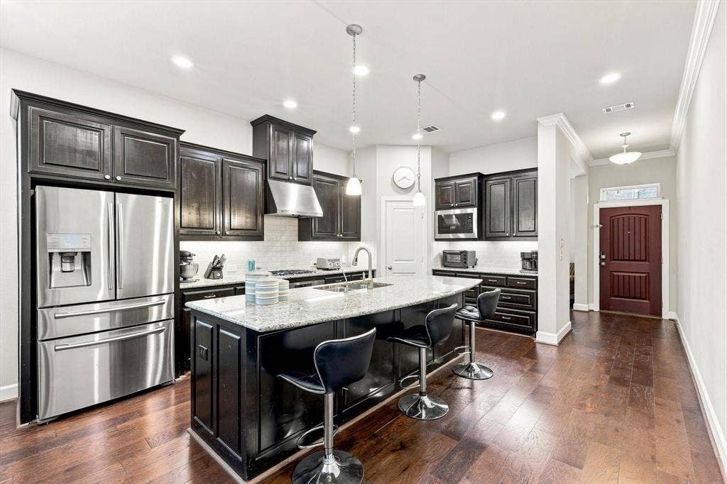 5441 Caine Road, Richardson, TX 75082 Gourmet kitchen with dark wood cabinetry, stainless steel appliances, a center island featuring a light-toned countertop, and recessed lighting