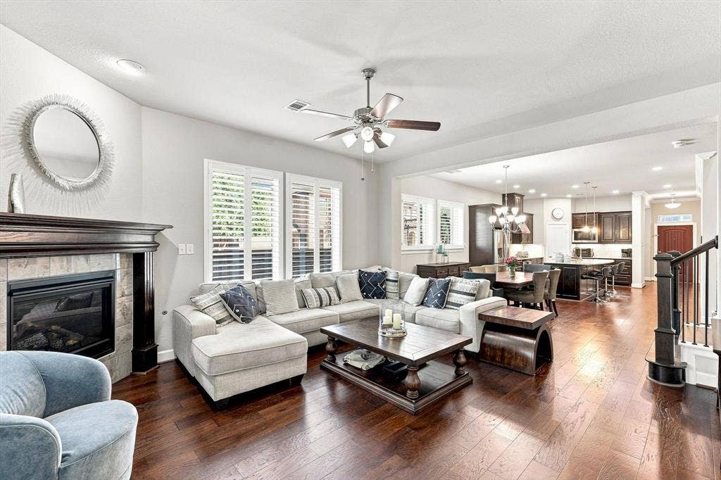 5441 Caine Road, Richardson, TX 75082 Hardwood flooring throughout, a gas fireplace with a decorative mantel, plantation shutters, a ceiling fan, and recessed lighting