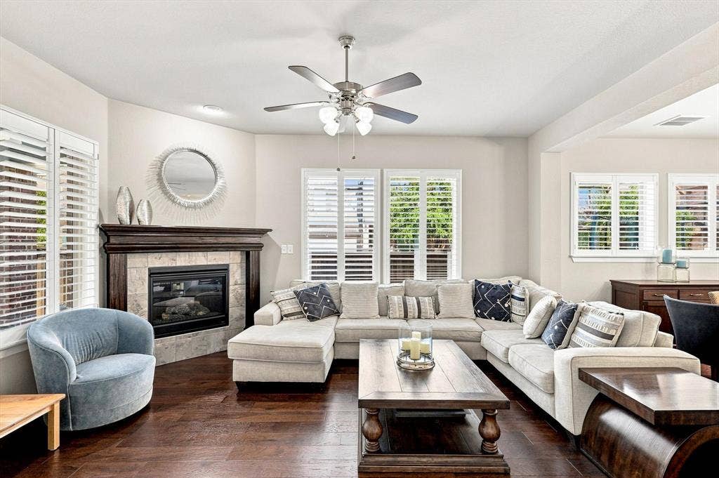 5441 Caine Road, Richardson, TX 75082 Living area featuring a corner fireplace with a wood mantel, wood-finish flooring, and white plantation shutters on multiple windows