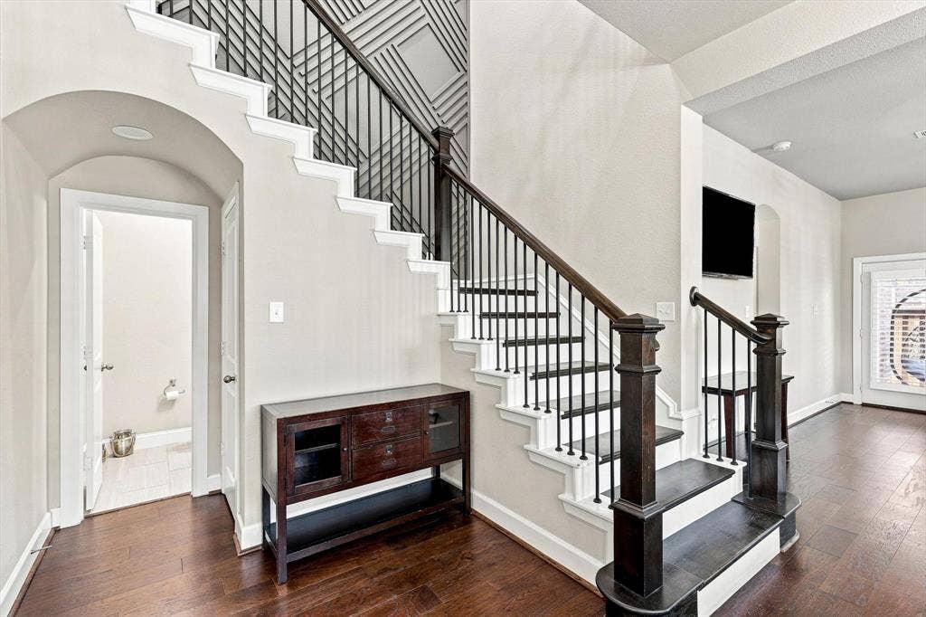 5441 Caine Road, Richardson, TX 75082 Rich wood-finish flooring, staircase with dark wood-finish handrail and black iron balusters, recessed lighting, arched doorway, and built-in wall niche
