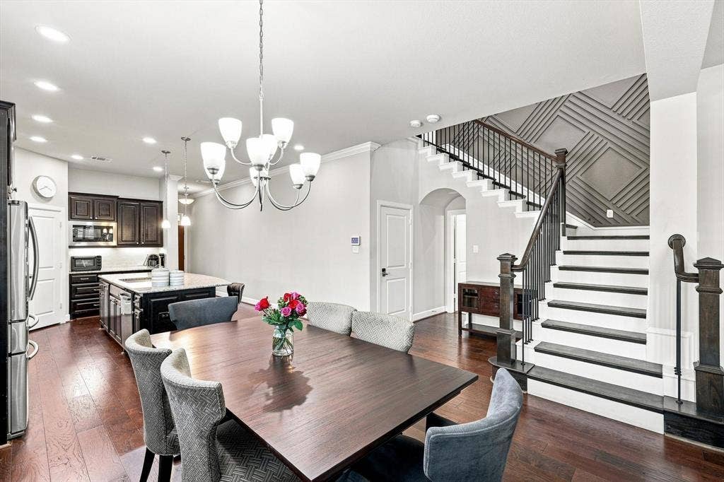 5441 Caine Road, Richardson, TX 75082 Hardwood flooring throughout, kitchen island with built-in storage, stainless steel appliances, chandelier lighting, and a staircase with decorative wall paneling