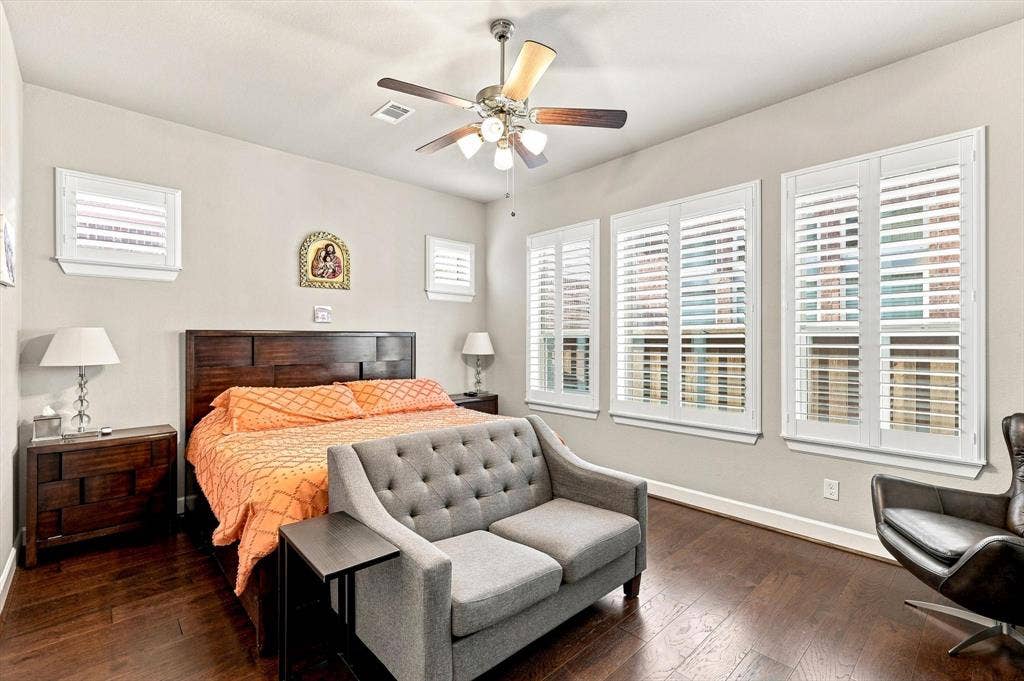 5441 Caine Road, Richardson, TX 75082 Wood-finish flooring, multiple windows with white shutters, ceiling fan with integrated lighting, and a wood-paneled headboard