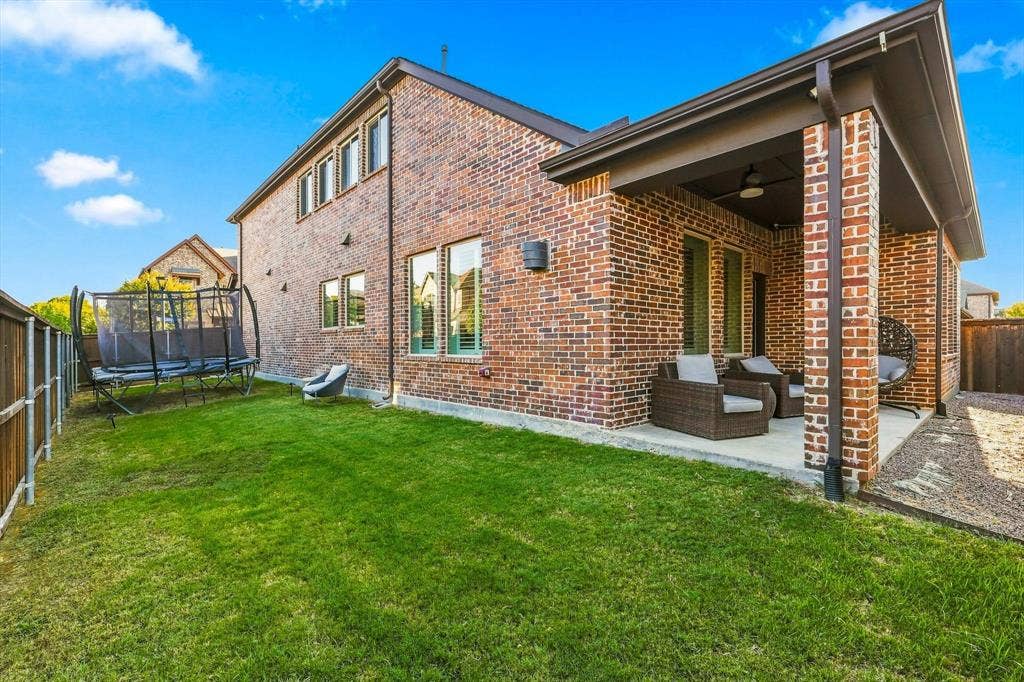 5441 Caine Road, Richardson, TX 75082 Brick exterior with multiple windows, covered patio with recessed lighting, and a fenced yard with a grass lawn