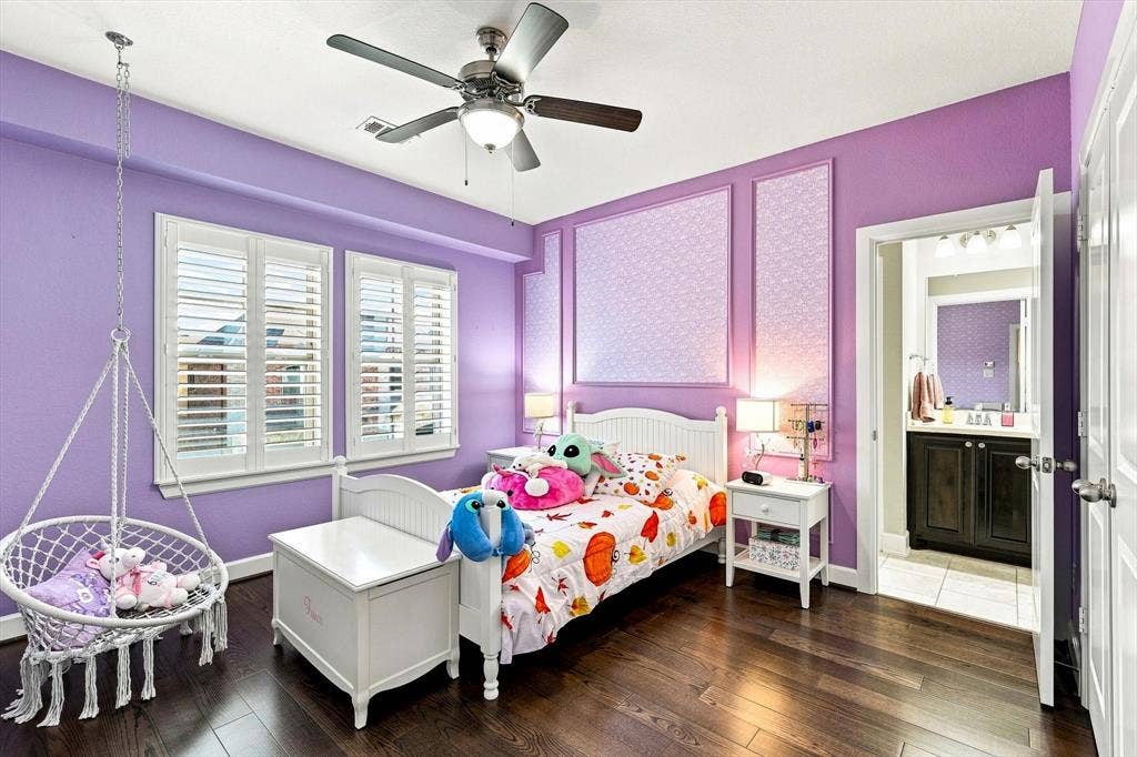 5441 Caine Road, Richardson, TX 75082 Wood-finish flooring, two windows with white louvered shutters, ceiling fan with integrated lighting, decorative wall panels, and an attached full bathroom with a dark wood-finish vanity