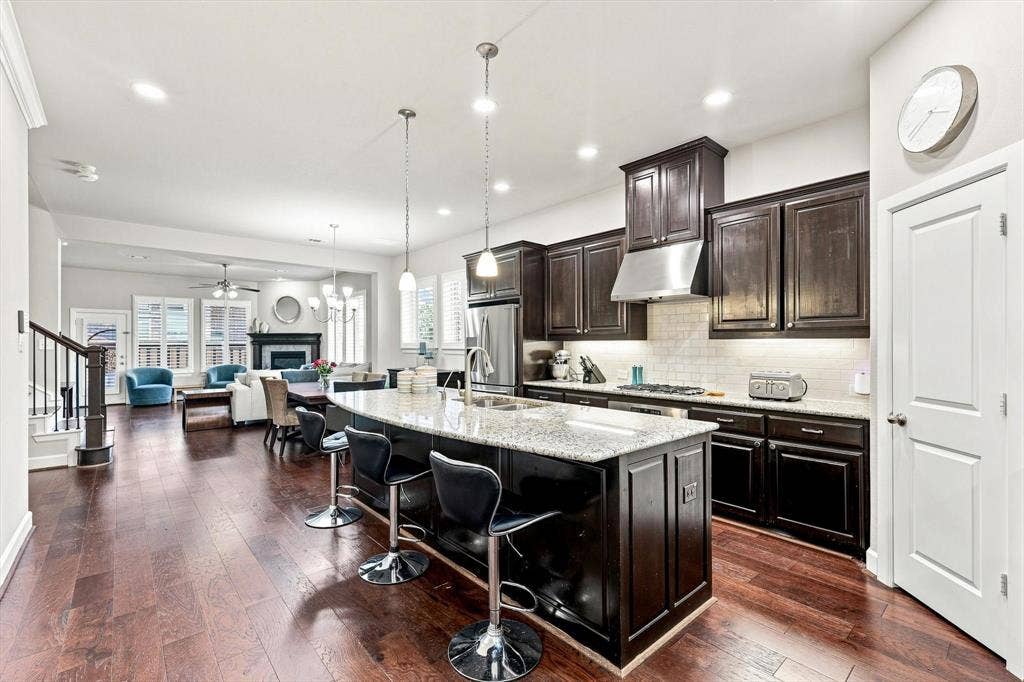 5441 Caine Road, Richardson, TX 75082 Expansive wood-finish flooring throughout, kitchen island with seating, stainless steel appliances, dark wood cabinetry, and a white subway tile backsplash