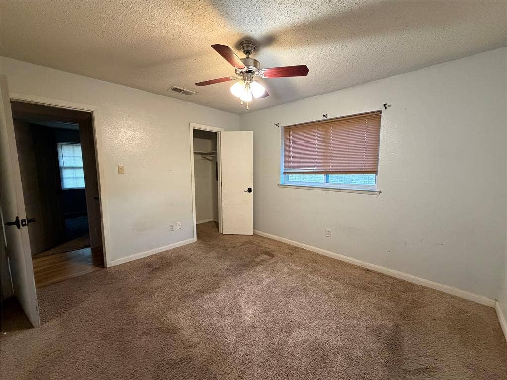 Ceiling fan with light fixture, window with blinds, brown carpeting, interior doors with dark hardware, and a closet