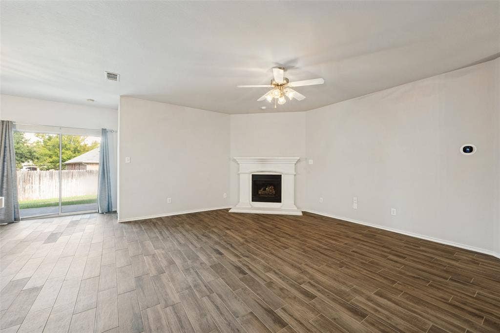 Wood-finish flooring, corner fireplace with white mantel, ceiling fan, and sliding glass door