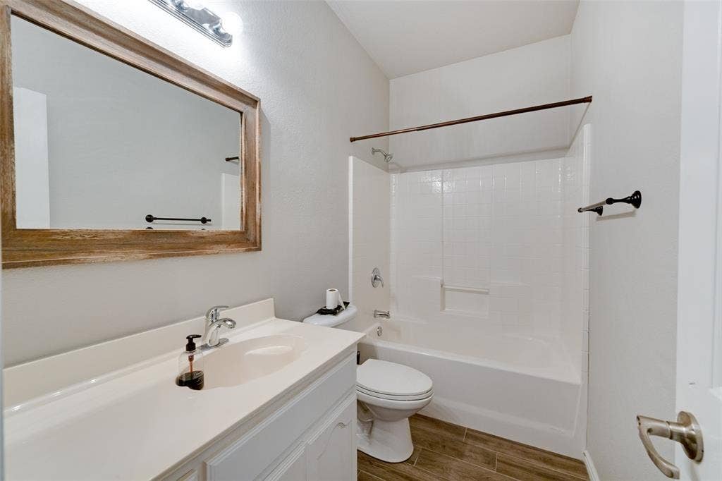 White vanity with integrated sink, wood-finish flooring, and a shower-tub combination