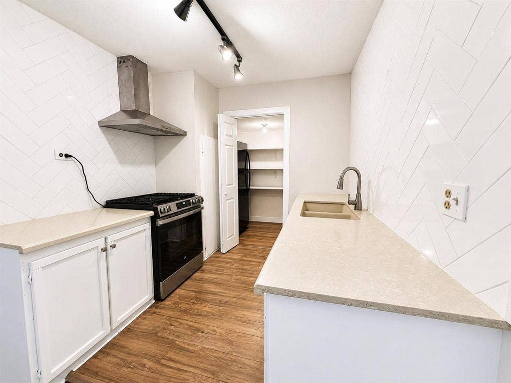 709 S Munger Boulevard, Dallas, TX 75223 White shaker-style cabinetry with light countertops, stainless steel range with matching vent hood, and wood-finish flooring