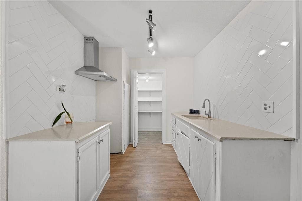709 S Munger Boulevard, Dallas, TX 75223 Galley kitchen featuring wood-finish flooring, white cabinetry, light-toned countertops, and a stainless steel range hood