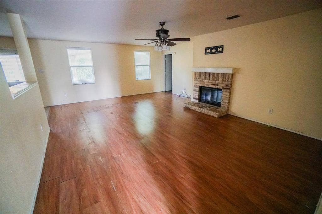 1517 Harvest Crossing Drive, Wylie, TX 75098 Spacious interior featuring wood-finish flooring, a brick-surround fireplace with a white mantel, multiple windows, and a ceiling fan with integrated lighting