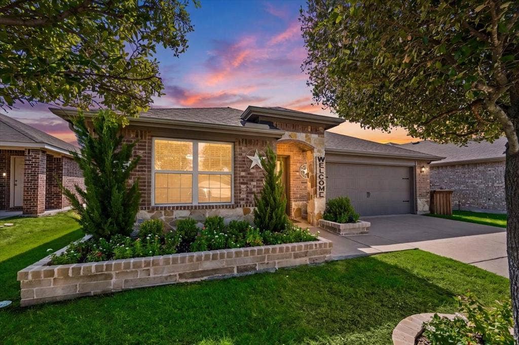 2225 Torch Lake Drive, Forney, TX 75126 Brick and stone facade with an attached garage, featuring a raised brick planter, mature landscaping, and a well-maintained lawn