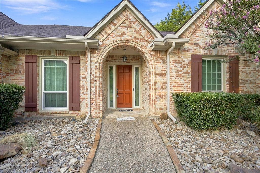 Brick facade, arched entry, panel front door, decorative shutters, stone-lined pathway