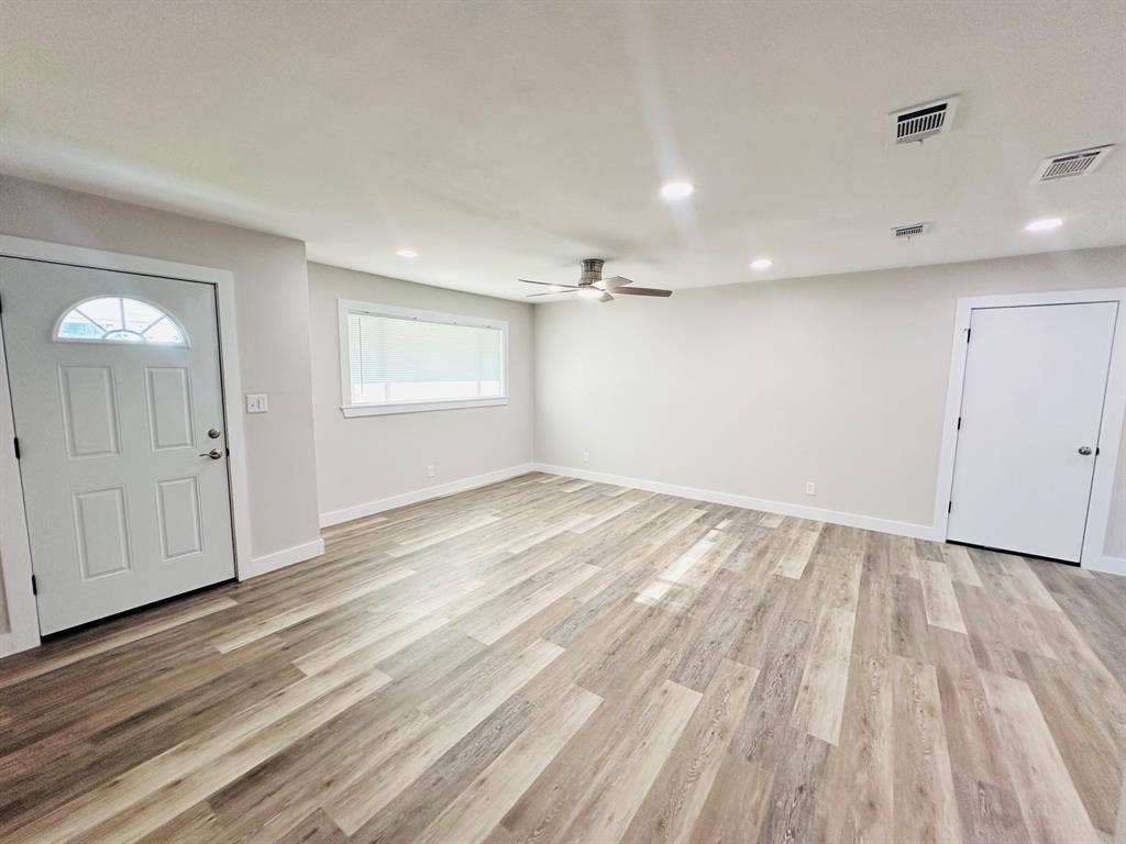 Wood-finish flooring throughout, recessed lighting, ceiling fan, white paneled door, and a horizontal window