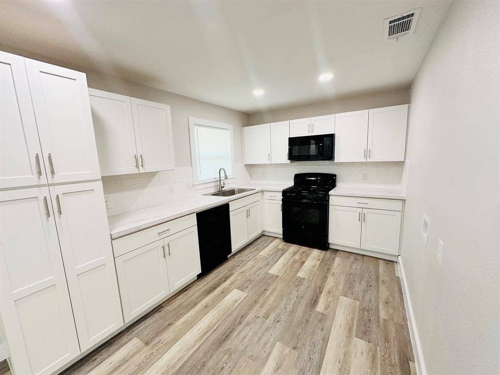 White shaker cabinetry, light-toned wood-finish flooring, white subway tile backsplash, recessed lighting, and stainless steel sink