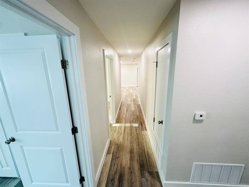 Hallway with wood-finish flooring, white paneled doors, and light-toned wall finishes