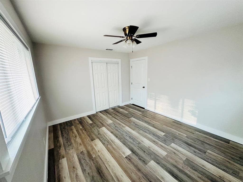 Wood-finish flooring, ceiling fan, window with blinds, and white bi-fold closet doors