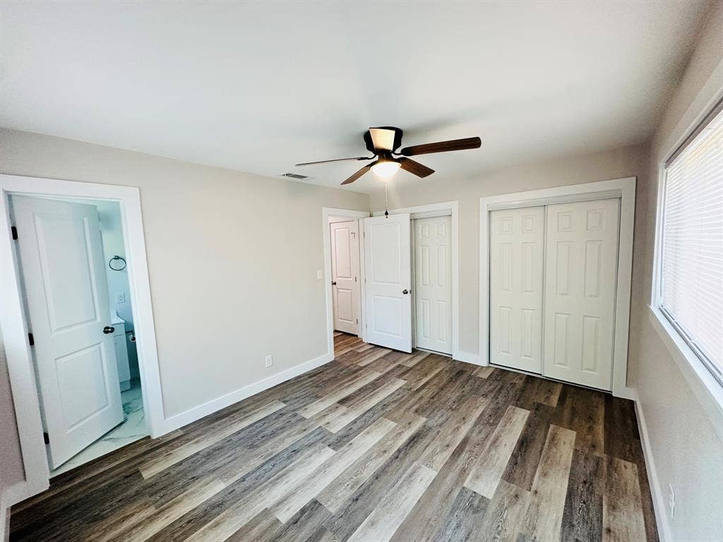 Wood-finish flooring throughout, white paneled doors, and a ceiling fan with integrated lighting