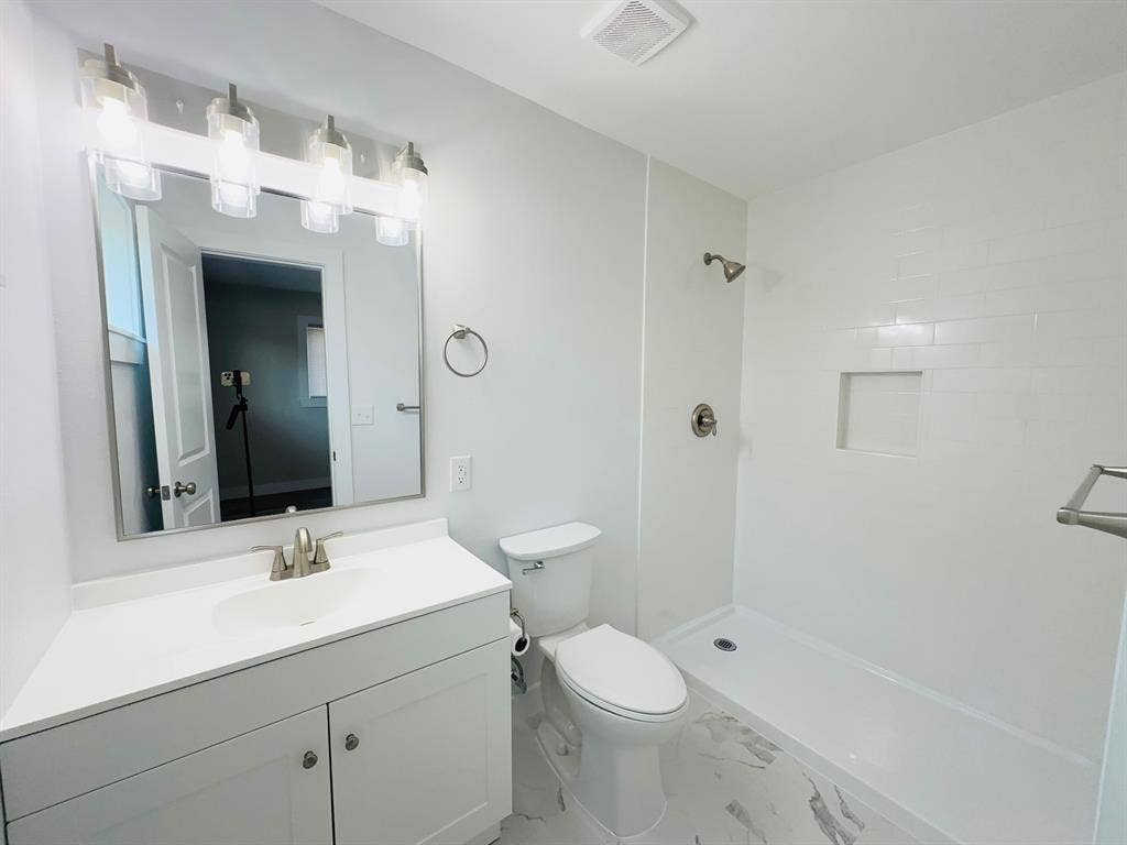 Modern bathroom with a walk-in shower, white subway tile surround, recessed shower niche, and a vanity with a white countertop