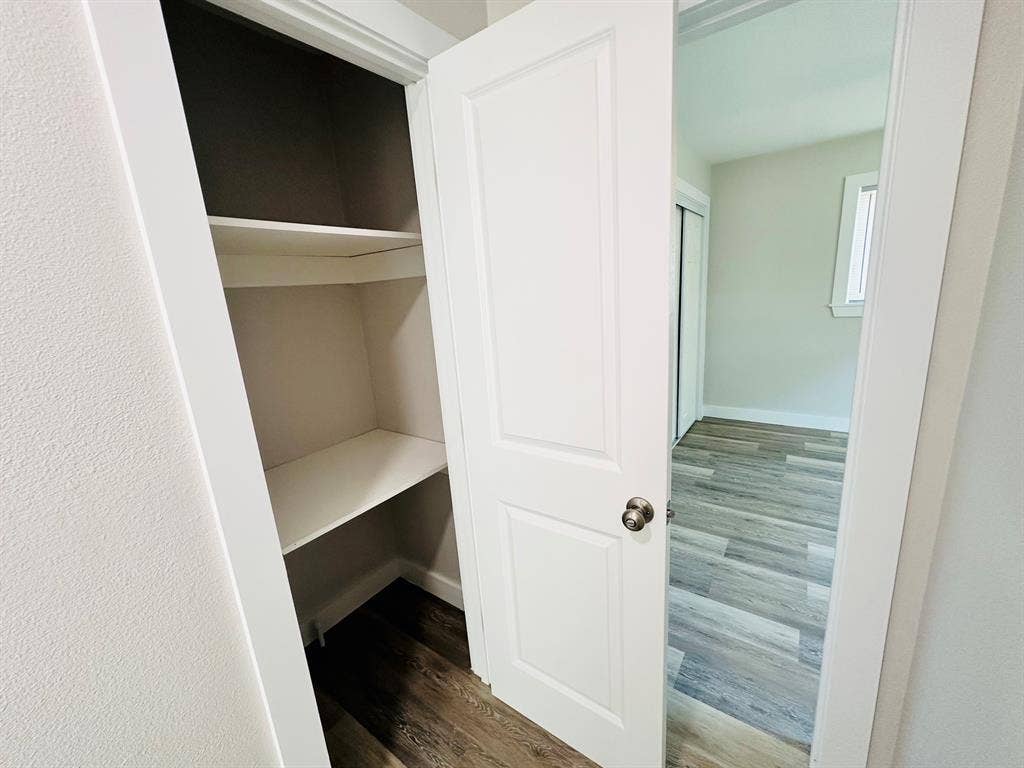 Built-in shelving, white paneled door, light-colored wood-finish flooring, white trim details, sliding closet doors