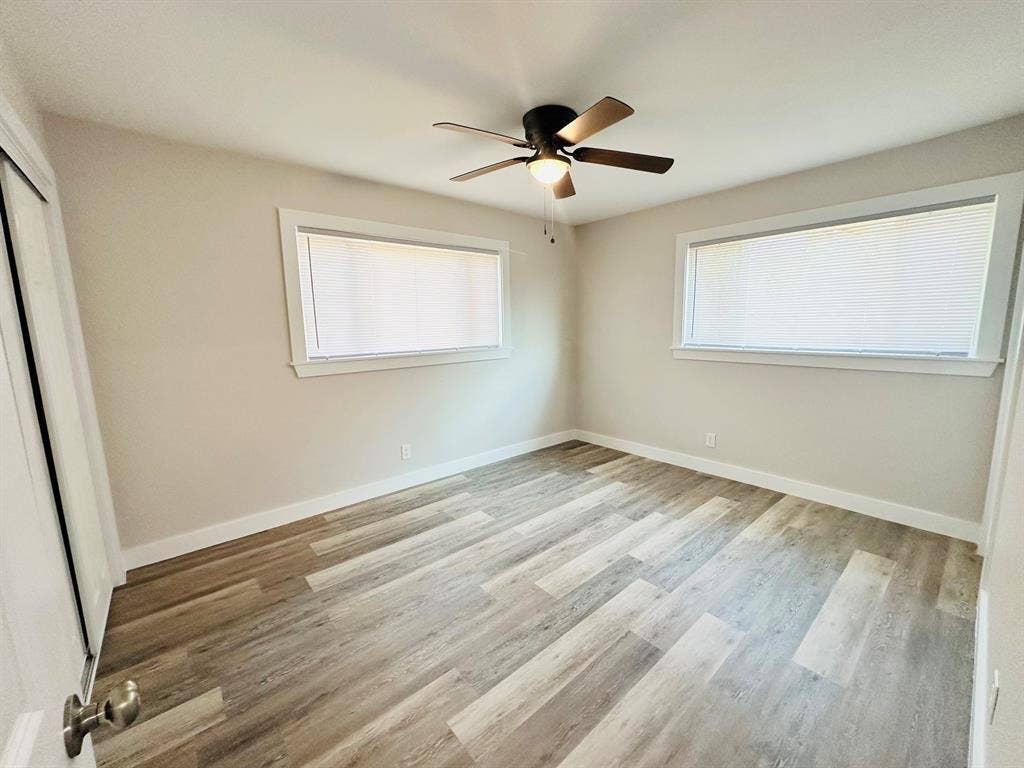 Room with wood-finish flooring, two large windows, and a ceiling fan with integrated lighting