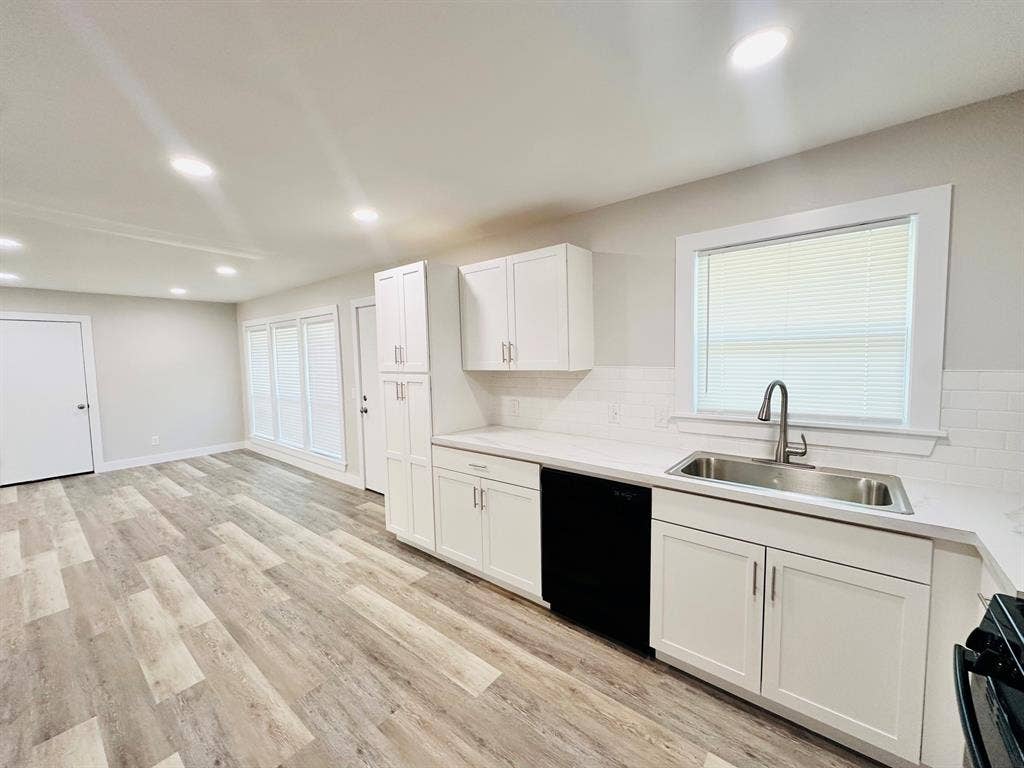 Light-toned wood-finish flooring, white shaker cabinetry, stainless steel sink, white subway tile backsplash, and recessed lighting