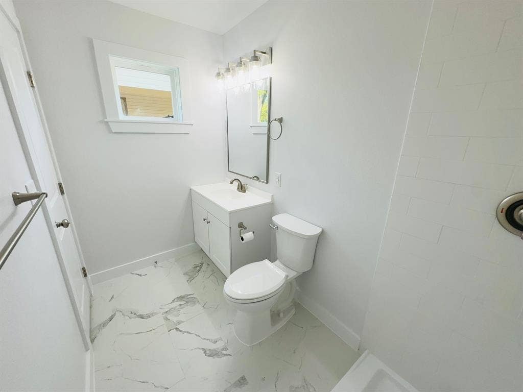 White vanity with integrated sink, rectangular mirror, light fixture, and patterned tile flooring