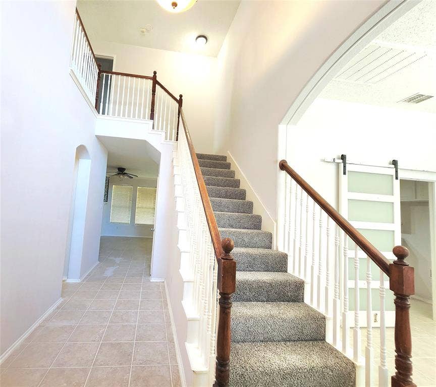 3625 Mason Drive, Plano, TX 75025 Two-story entryway featuring carpeted stairs with wood newel posts and banister, an arched doorway, and tile flooring