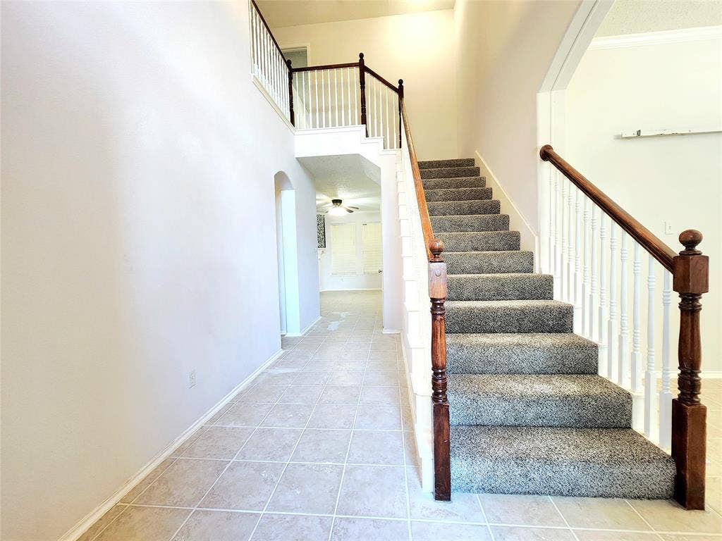 3625 Mason Drive, Plano, TX 75025 Two-story entryway featuring tile flooring, a carpeted staircase with wood handrails, and a second-story landing with a white spindle railing