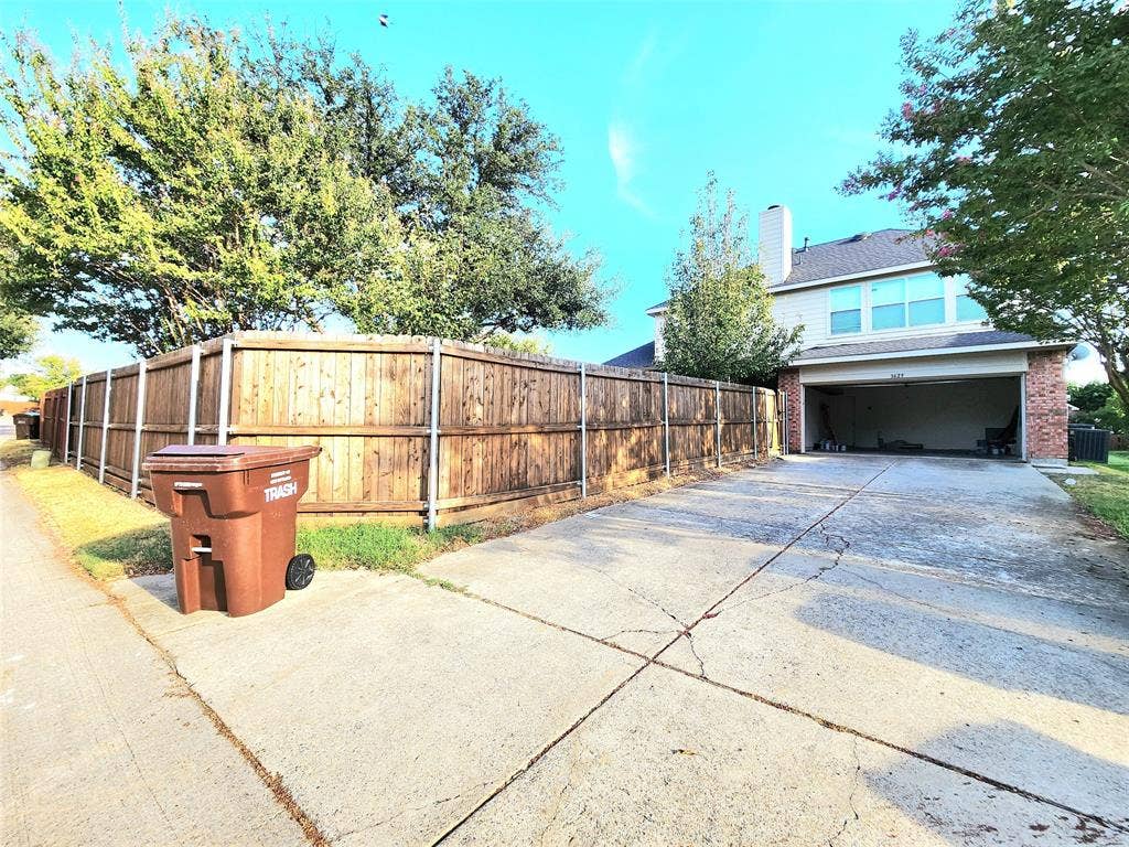 3625 Mason Drive, Plano, TX 75025 Attached two-car garage with a concrete driveway, brick facade, and wood fencing