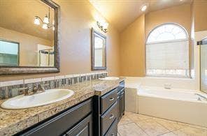 Bathroom with a bath, healthy amount of natural light, tile patterned flooring, vaulted ceiling, and vanity