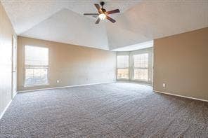 Carpeted empty room featuring vaulted ceiling, baseboards, and ceiling fan