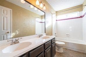 Full bath with toilet, double vanity, and tub / shower combination