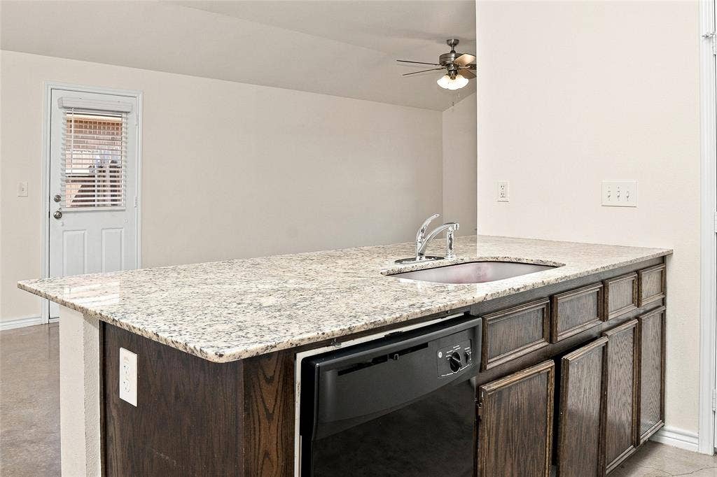 6015 Amelia Earhart Boulevard, #B, Killeen, TX 76543 Kitchen island with granite countertop, stainless steel sink, dark wood-finish cabinetry, and built-in dishwasher
