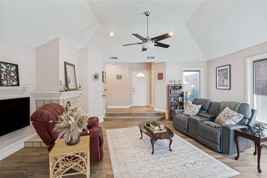 Vaulted ceiling with a ceiling fan, wood-finish flooring, and a tiled fireplace surround