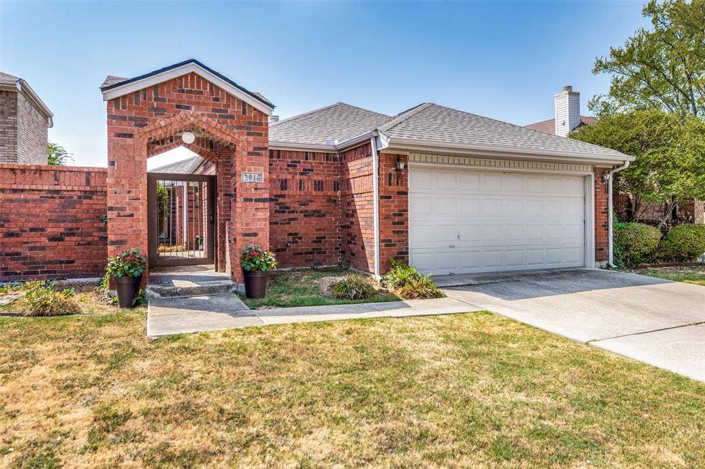 Brick exterior with an arched entryway, wrought iron gate, attached garage, and concrete driveway