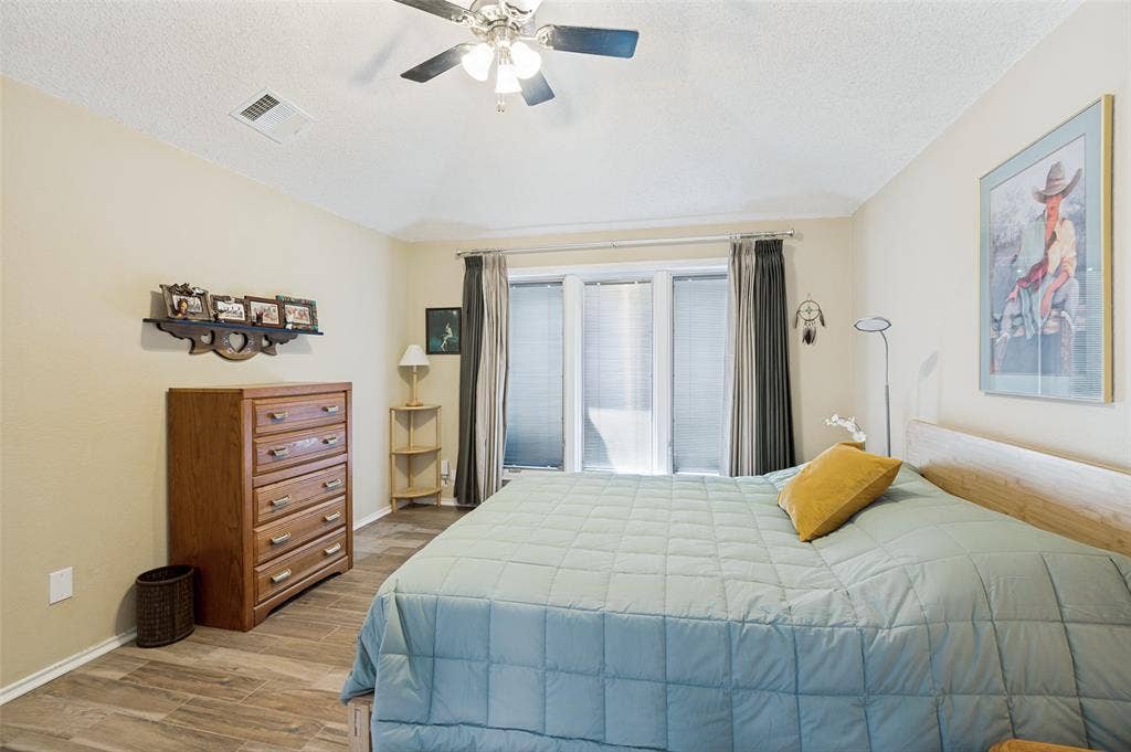 Wood-finish flooring, ceiling fan, and large windows with blinds and curtains