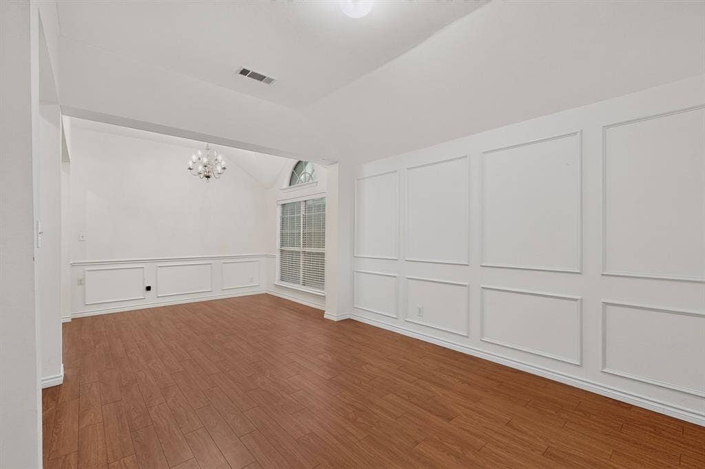 8108 Case Drive, Plano, TX 75025 Wood-finish flooring, accent wall paneling, vaulted ceiling, arched window, and a built-in chandelier