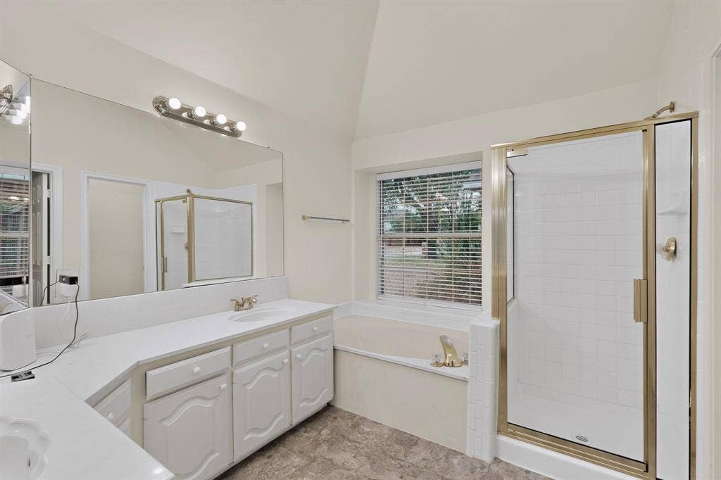 8108 Case Drive, Plano, TX 75025 Vaulted ceiling with overhead lighting, large vanity mirror, white cabinetry with integrated sinks, and a walk-in shower with a gold-tone frame